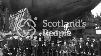 Staff of J & G Thomson posing before the bow of HMS Ramilies on the slip way on the day of the launch.