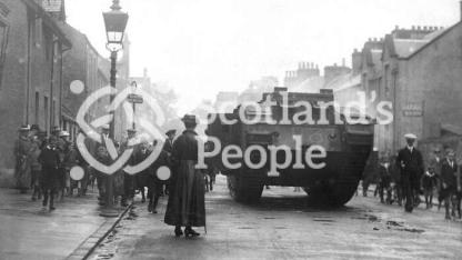 World War 1 Mk V (Male) Tank in Callander high street with crowds and woman in foreground