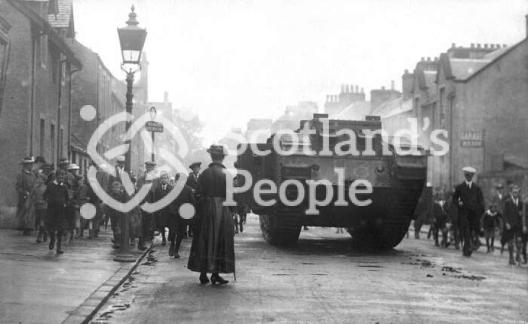 World War 1 Mk V (Male) Tank in Callander high street with crowds and woman in foreground
